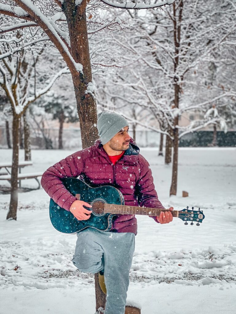 Stock image of a man playing acoustic guitar outside in the snow.