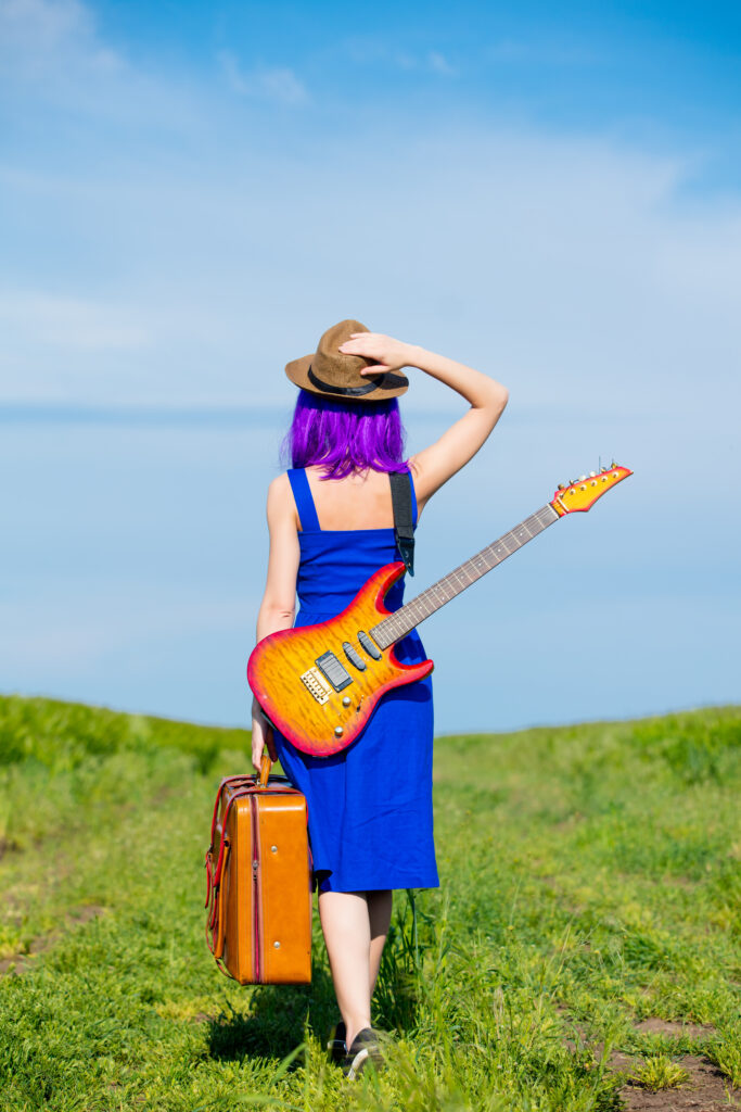 Woman in a field with an electric guitar and suitcase.