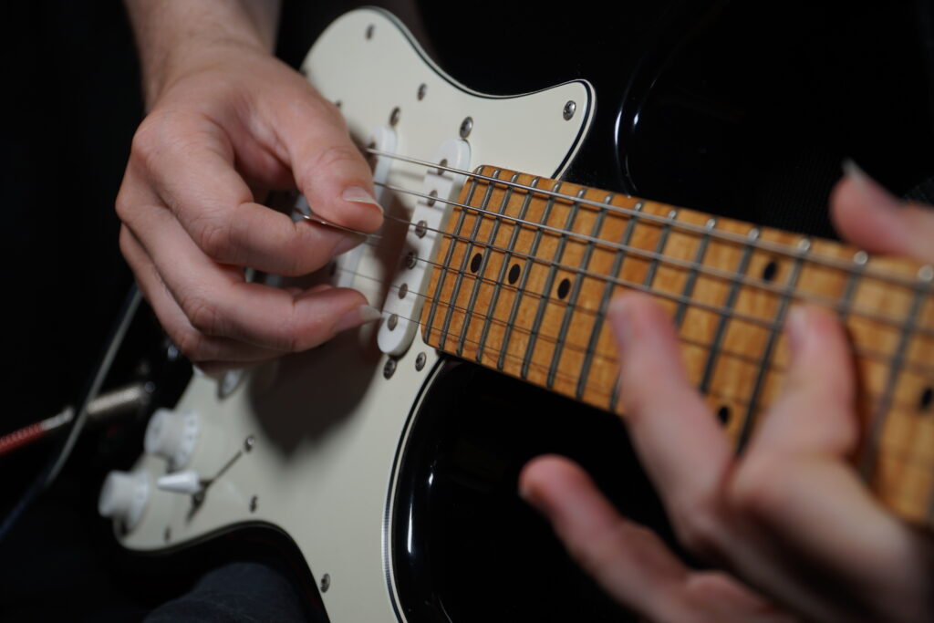 Close-up of a person playing a black Stratocaster with a maple fretboard.