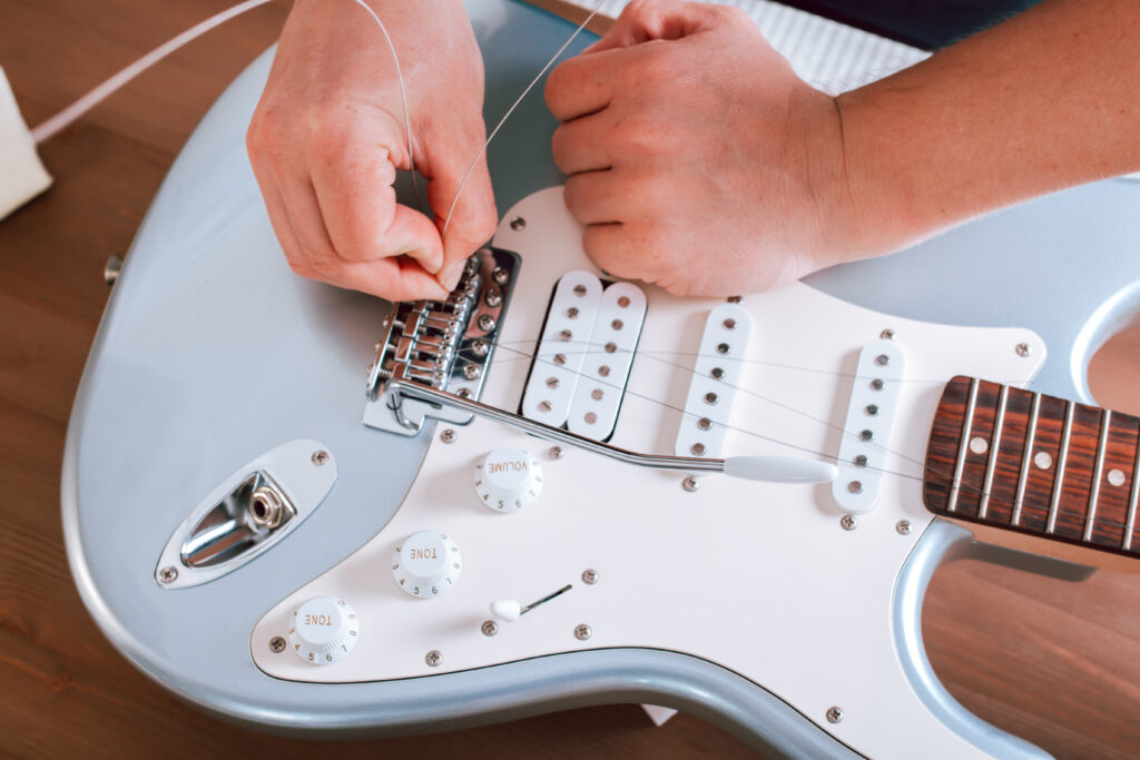 Stock image of someone putting new guitar strings on a blue Stratocaster-style guitar.