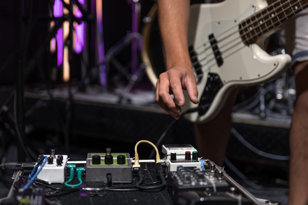 Stock image of a bassist grabbing an effects pedal on stage.
