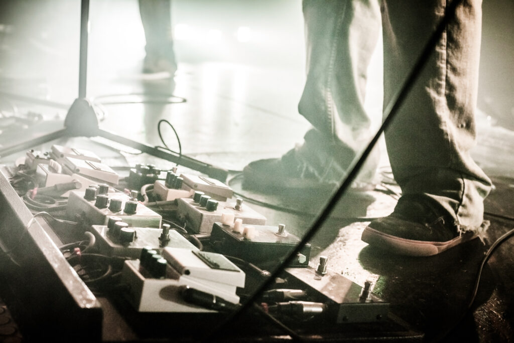 Hazy photo of a guitarist's effects pedals on stage.