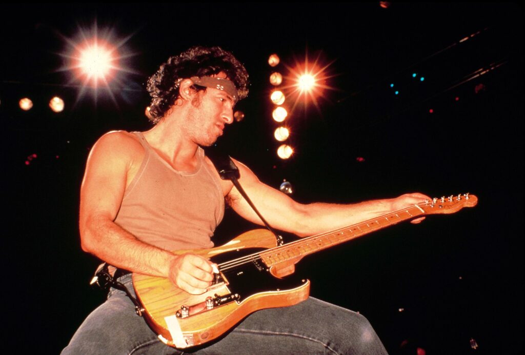Live photo of Bruce Springsteen wearing a vest and holding his Fender Telecaster guitar.
