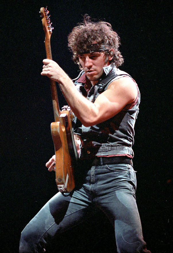 Bruce Springsteen on stage wearing a bandanna and holding a guitar.